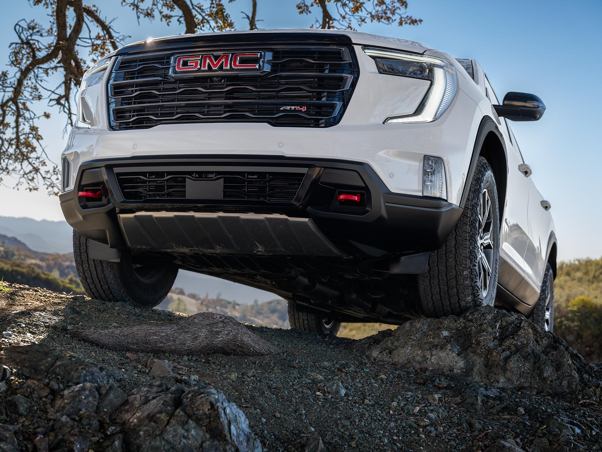 Vue de face d’un VUS GMC Acadia blanc 2027 avec le logo GMC sur la calandre, stationné sur des rochers irréguliers.