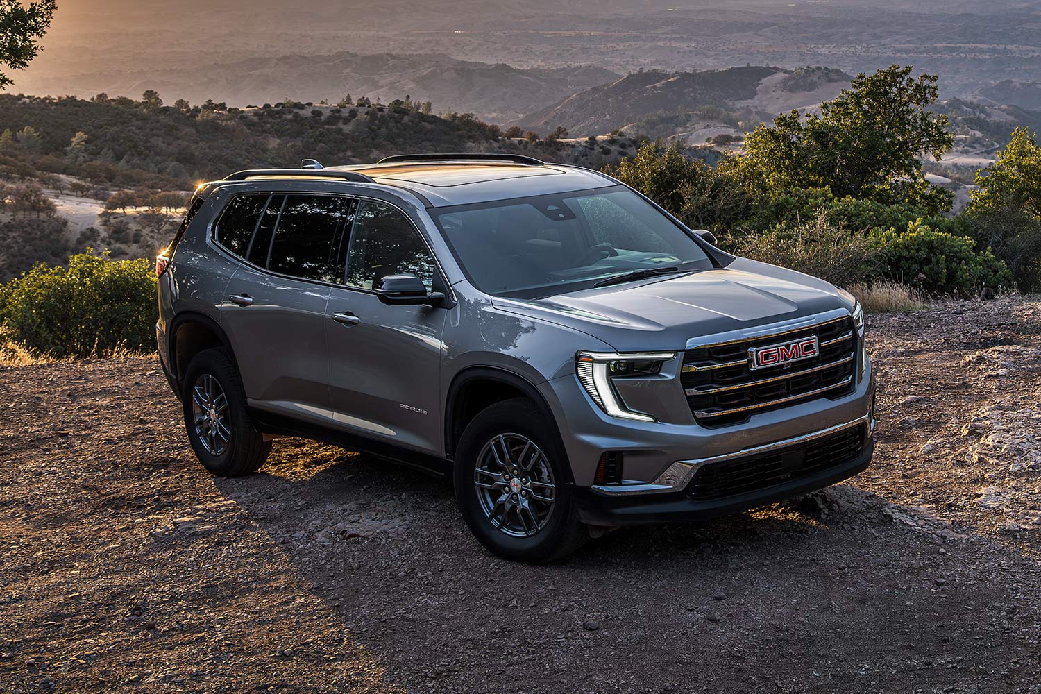 VUS GMC Acadia 2027 gris stationné sur un sentier de terre surplombant une vallée pittoresque avec des montagnes au loin.