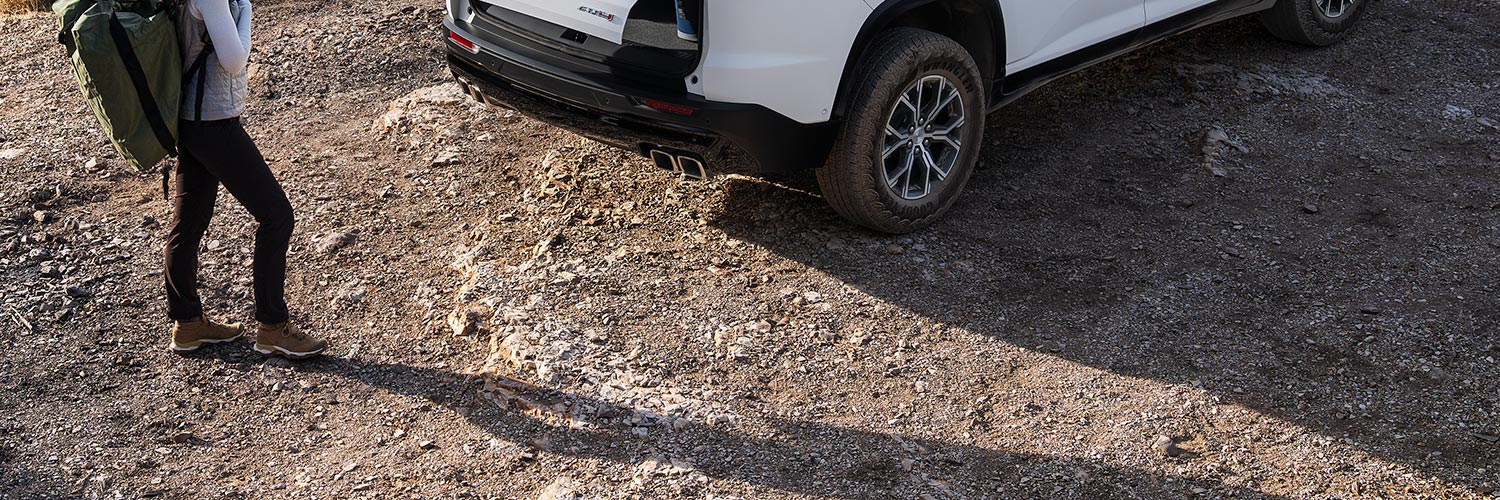 Une femme avec un sac à dos de randonnée, s’approchant d’un VUS GMC Acadia 2027 avec le coffre ouvert.
