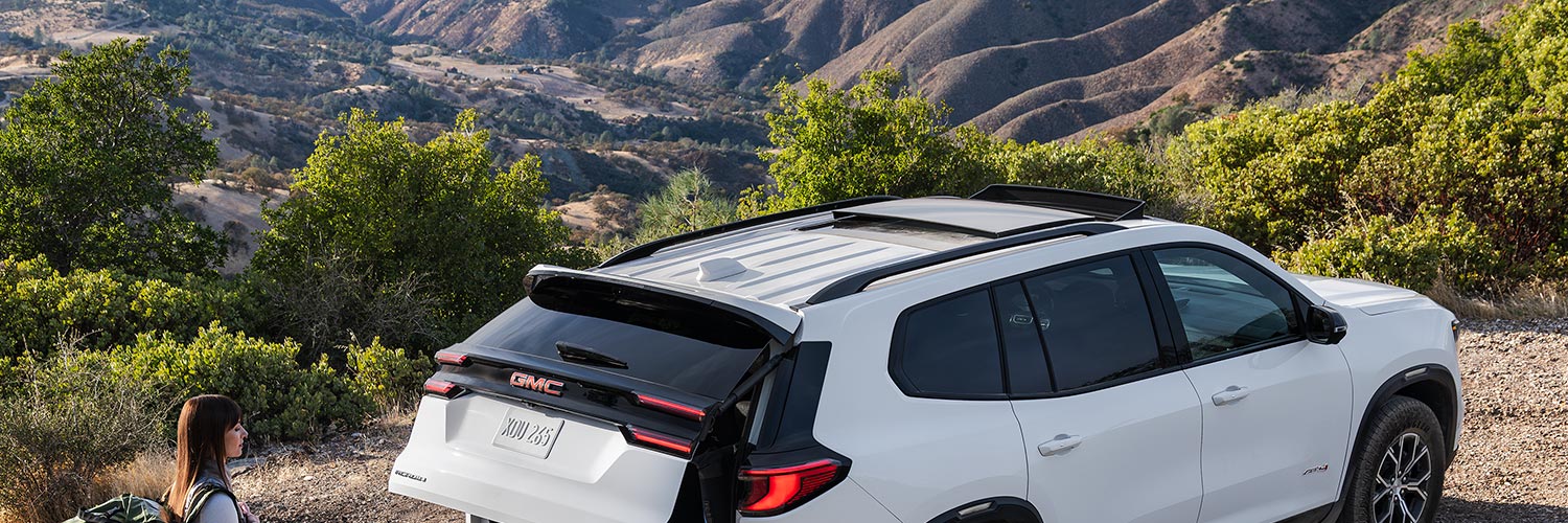 Une femme avec un sac à dos de randonnée, s’approchant d’un VUS GMC Acadia 2027 avec le coffre ouvert.