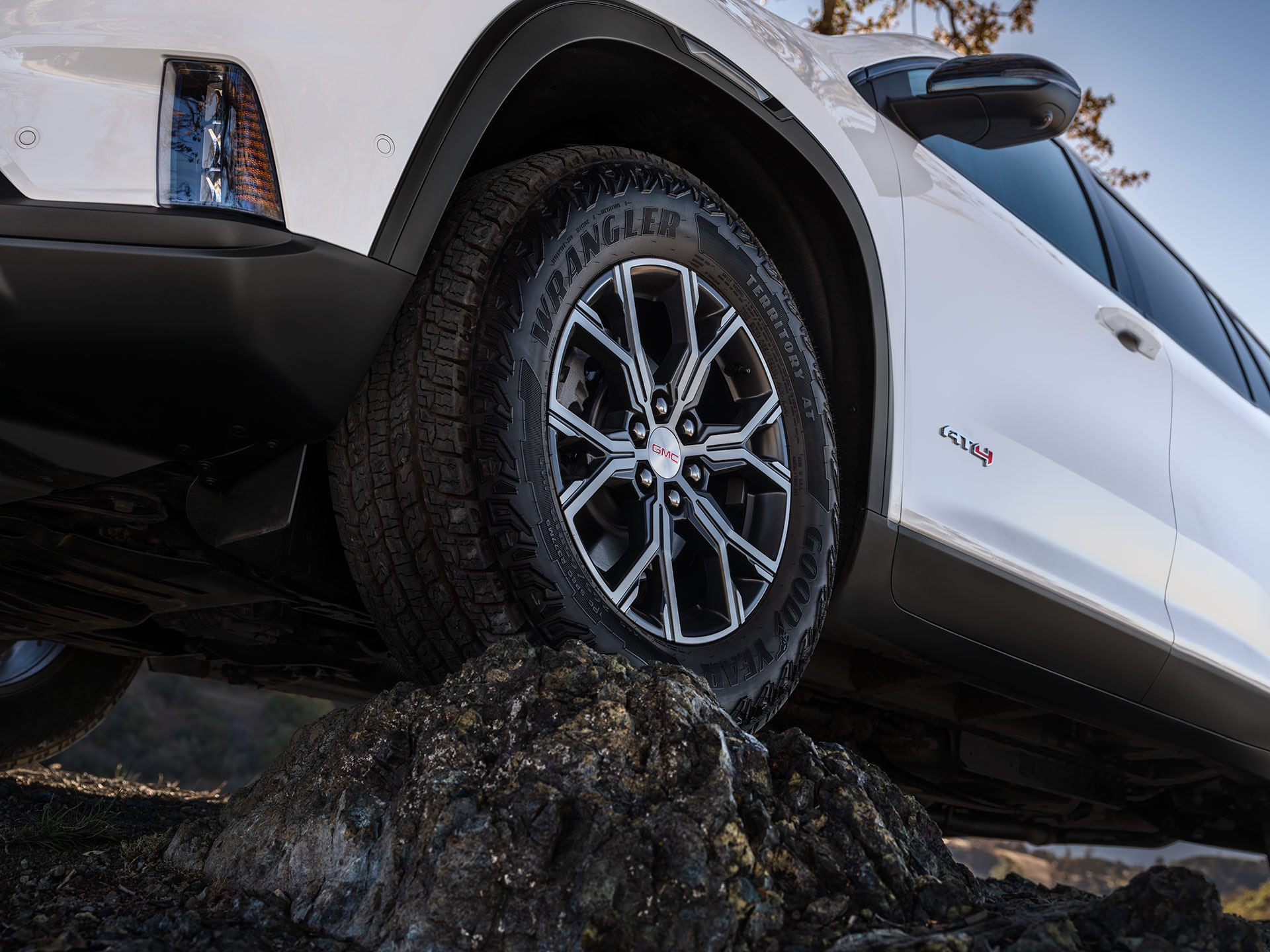 Gros plan d’un VUS GMC Acadia 2027 avec un pneu Goodyear Wrangler Territory AT grimpant par-dessus des rochers.