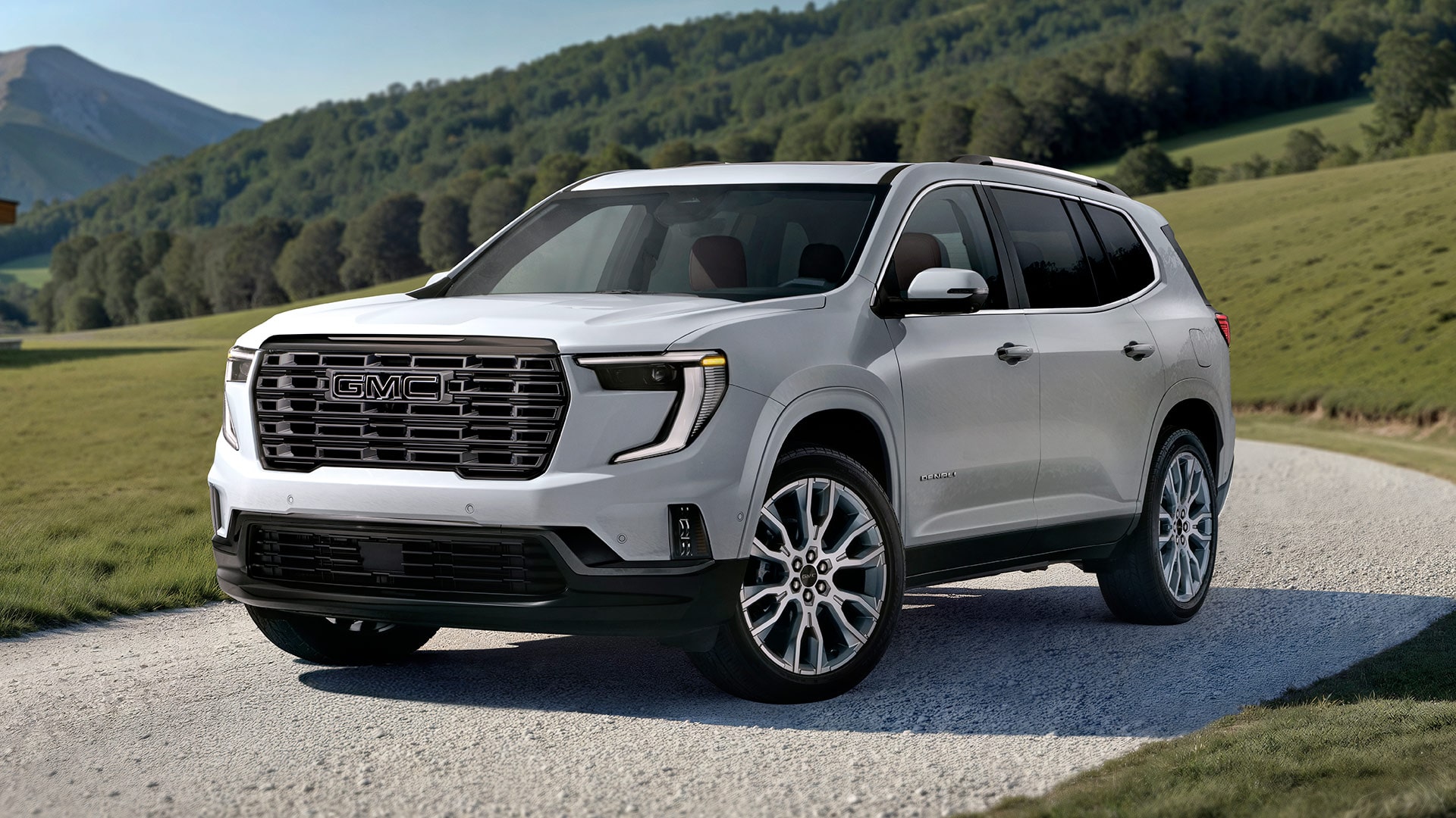 VUS GMC Acadia blanc 2027 stationné sur un chemin de gravier avec des collines verdoyantes ondulantes en arrière-plan, sous un ciel dégagé.