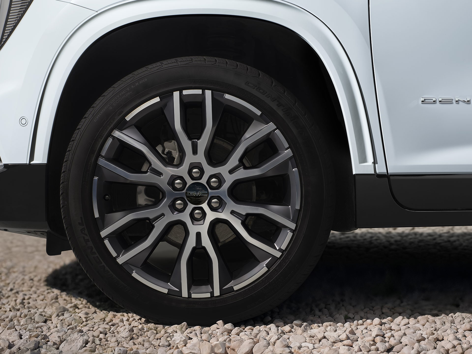 Plan rapproché d’une roue et d’un pneu à rayons multiples sur un véhicule blanc GMC Acadia Denali 2027 sur gravier.