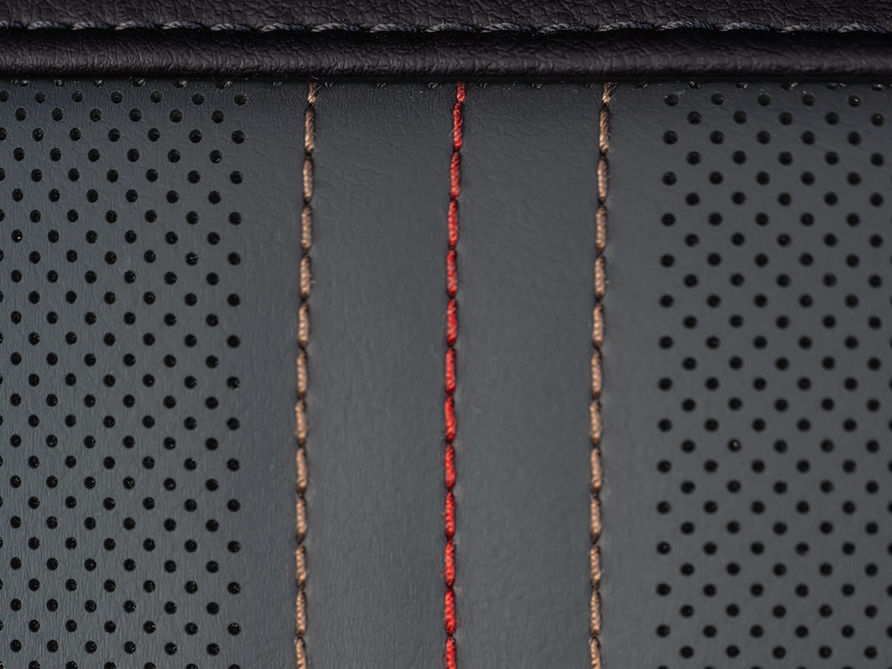 Vue rapprochée du cuir perforé gris foncé avec des coutures verticales rouges et beiges sur les sièges du VUS GMC Acadia AT4 2027.