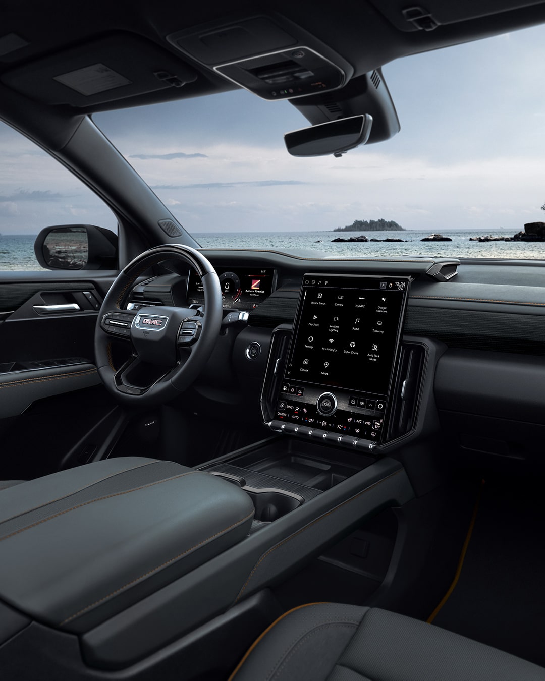 Vue côté passager du siège conducteur et du tableau de bord d’un VUS GMC Acadia 2027 avec un plan d’eau et des arbres au loin.