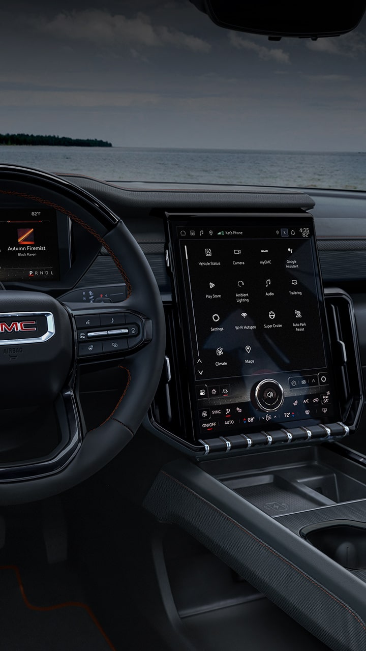 L’intérieur d’un VUS GMC Acadia 2027, mettant en valeur le volant avec le logo GMC et le grand système d’affichage numérique intégré.