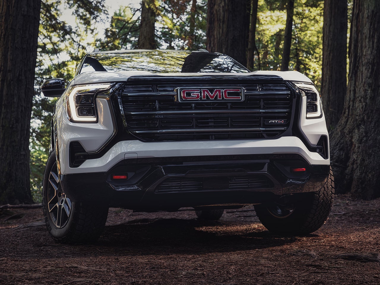 Vue de face d’un SUV AT4 GMC Terrain blanc 2027 avec une calandre distinctive et des phares lumineux, garé sur un sentier forestier.