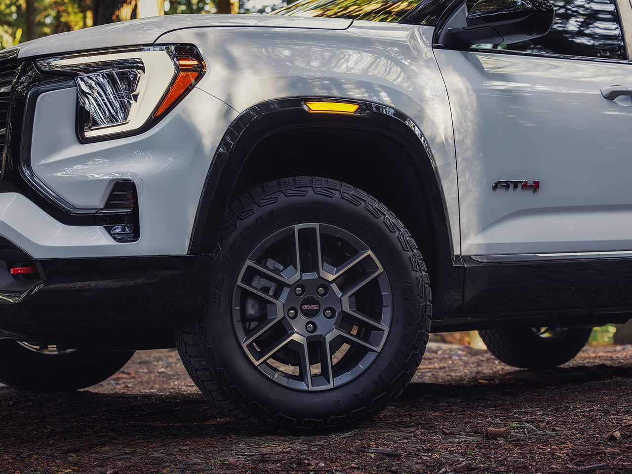 Un gros plan de la roue avant et de l’aile d’un SUV AT4 GMC Terrain blanc 2027 montrant le pneu tout-terrain et le logo de la roue GMC Terrain 2027.