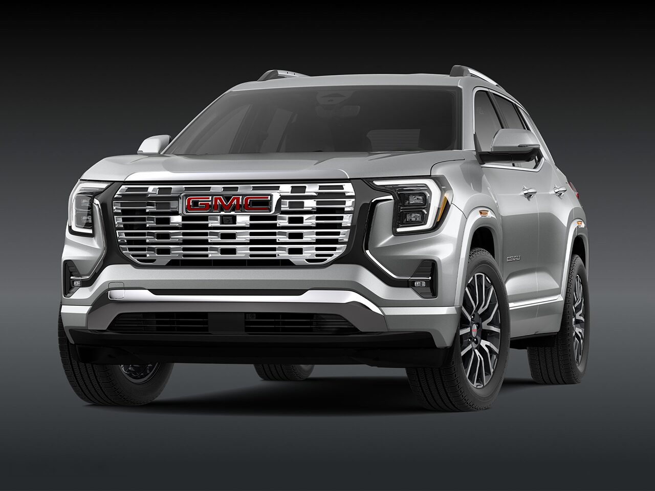A Front Three-Quarter View of the Silver 2026 2027 GMC Terrain Denali SUV on a Dark Background.