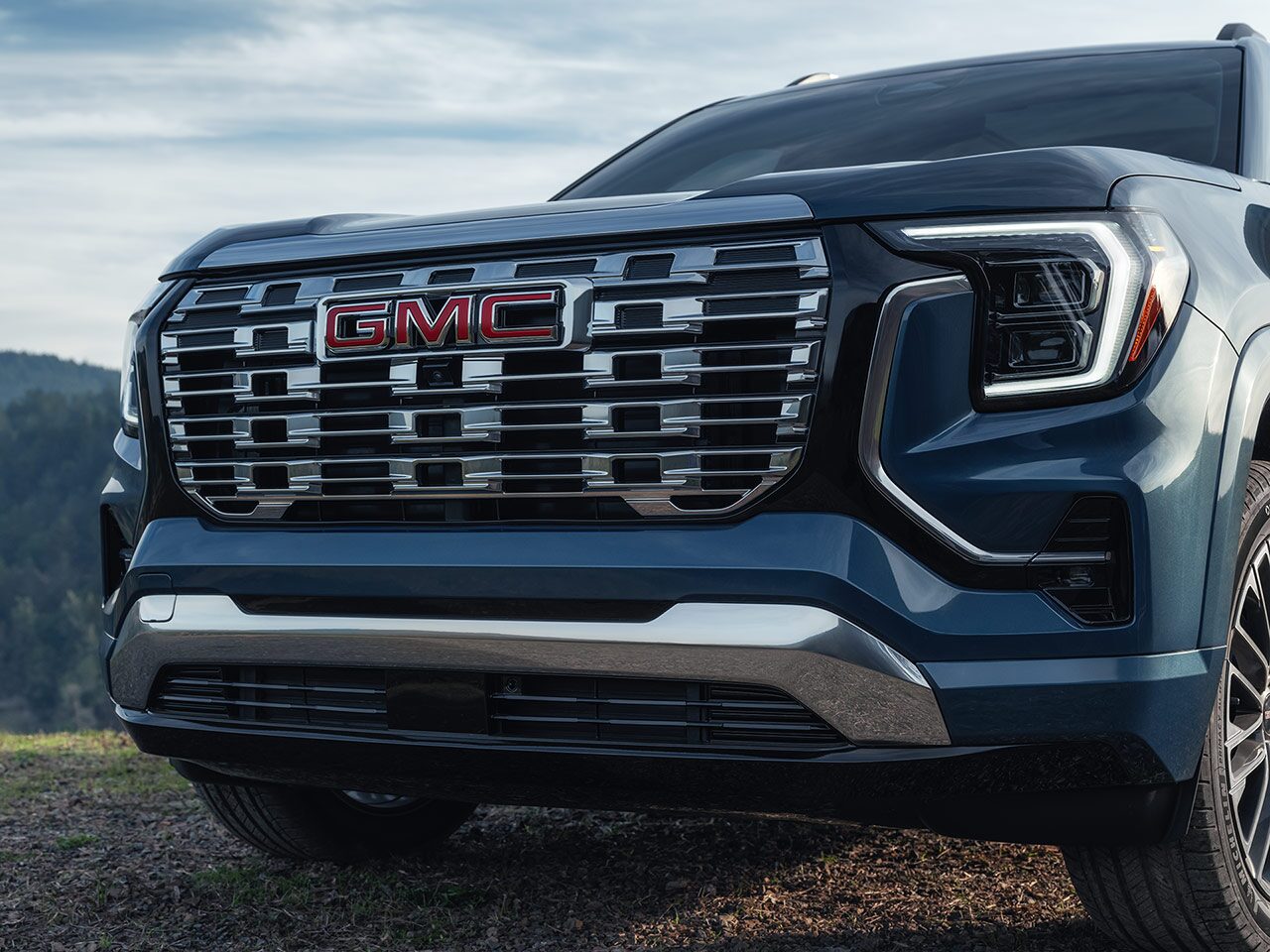 The Front Grille of a Dark Blue 2027 GMC Terrain SUV Featuring the Red 2027 GMC Terrain Logo and Bright Led Headlights.