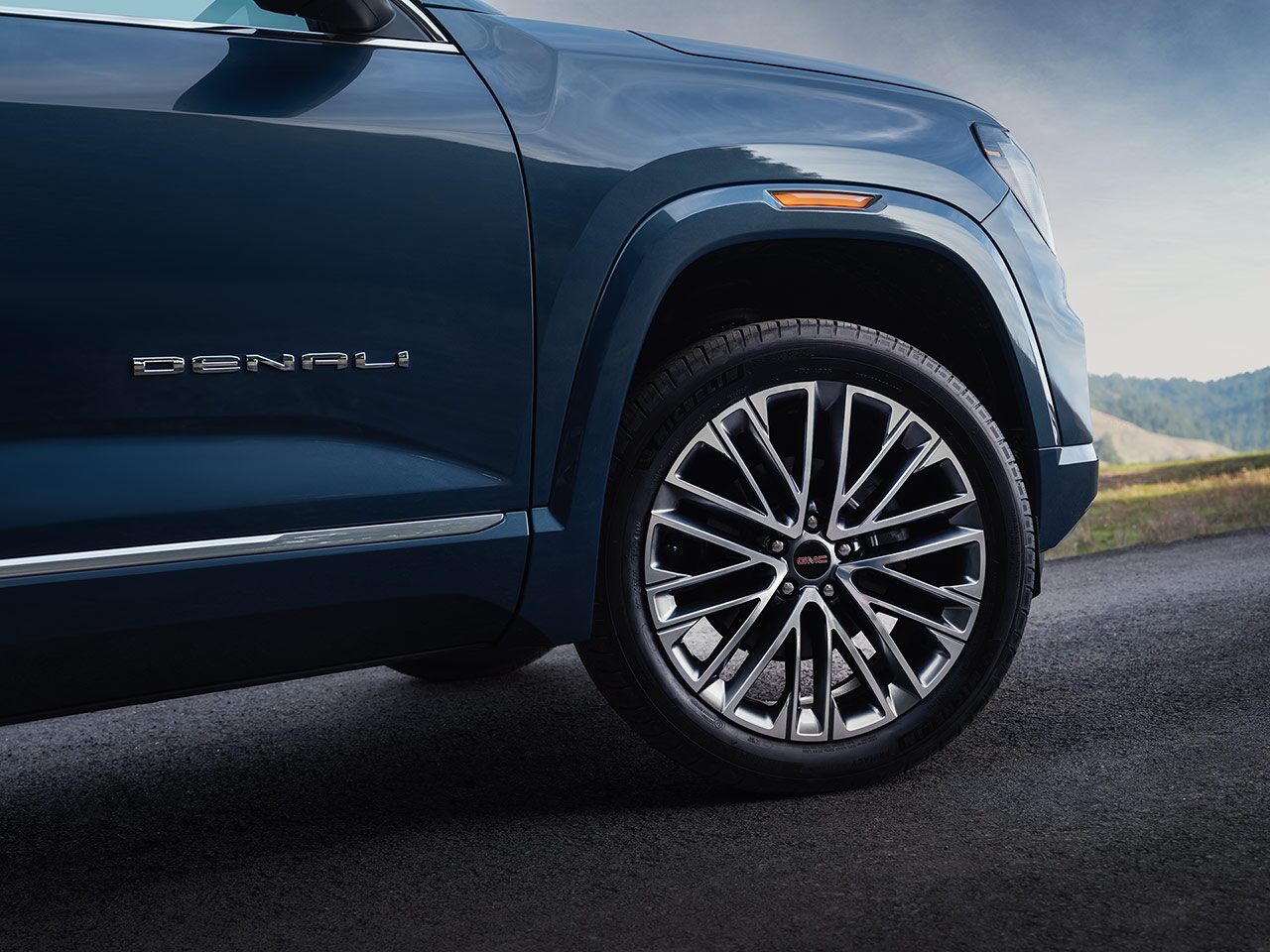 A Close-up of the Wheel and Fender of a Dark Blue 2027 GMC Terrain Denali SUV with the Denali Badge.