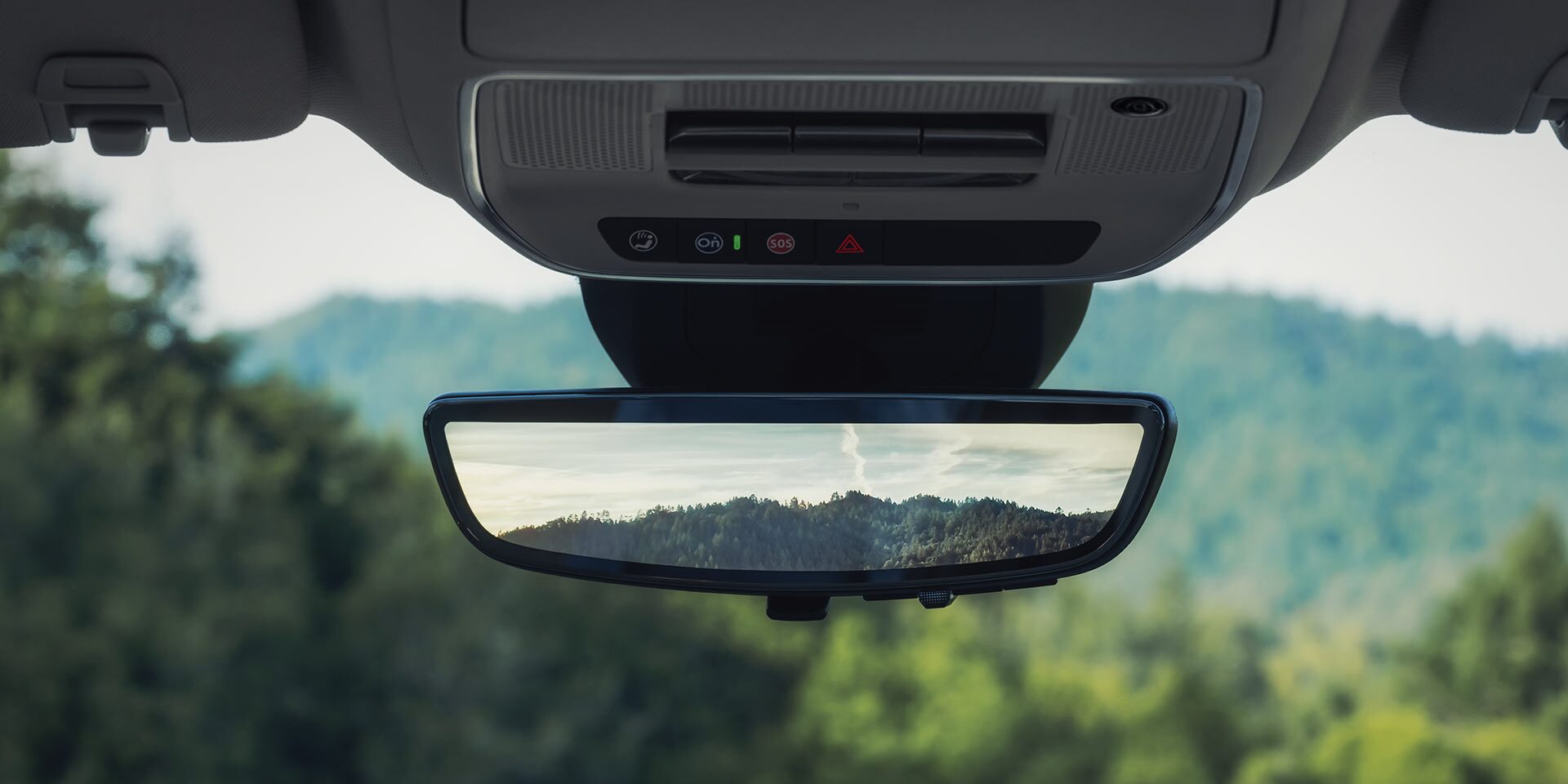 An Interior View of a 2027 GMC Terrain Vehicle with the Rearview Mirror Reflecting a Green Mountain Landscape.
