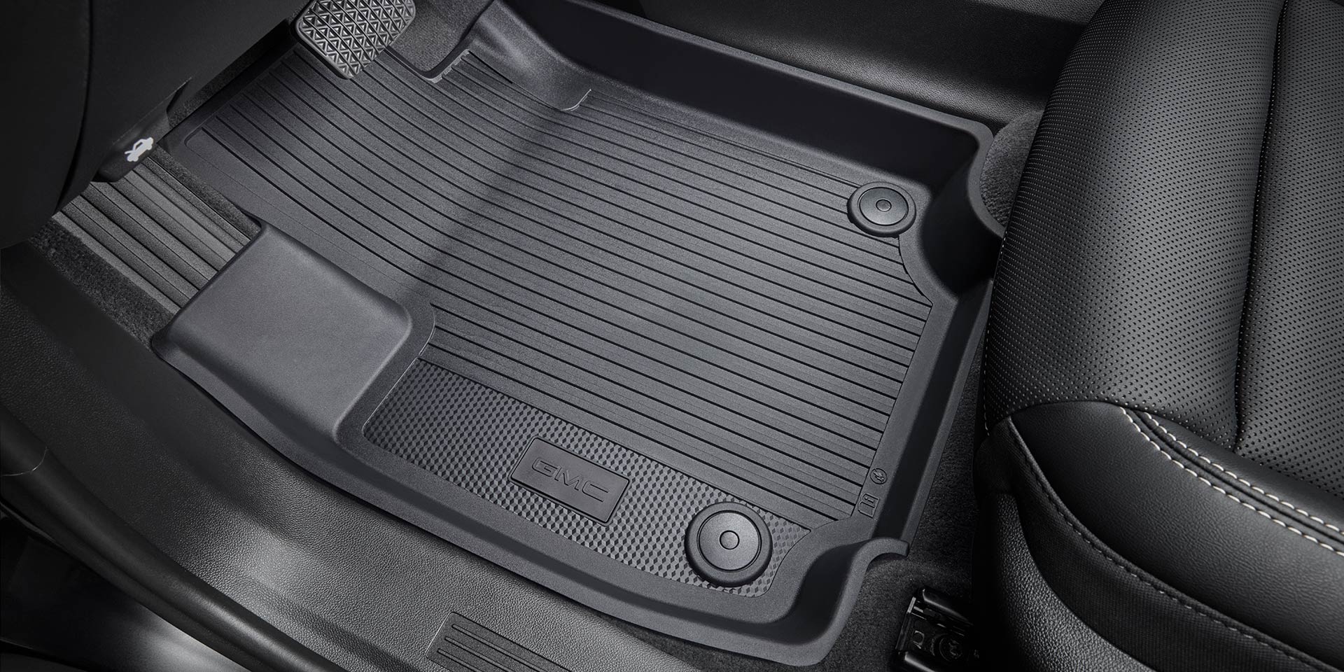 Vue rapprochée d’un tapis de sol noir GMC Terrain 2027 pour tous les temps, avec une texture nervurée et le logo GMC Terrain 2027 embossé dessus, à côté d’un siège en cuir noir avec des coutures blanches.