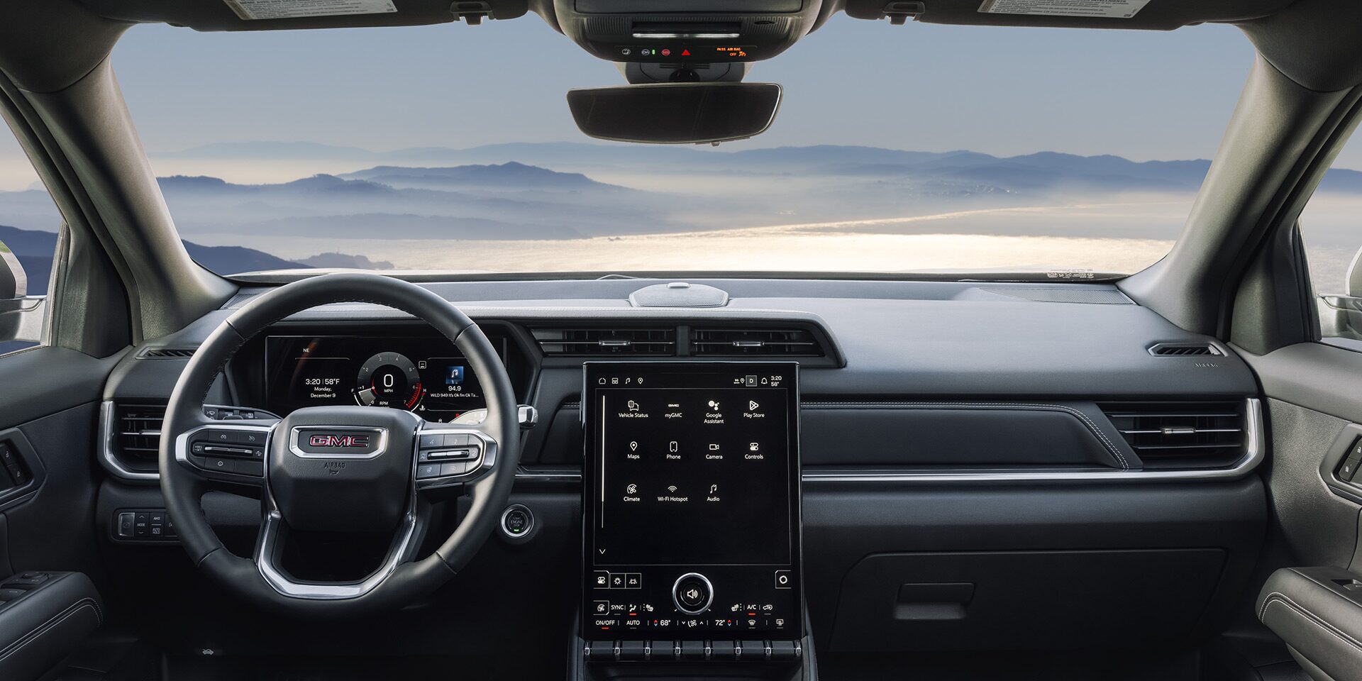 Interior View of a 2027 GMC Terrain Dashboard with Steering Wheel and Infotainment Screen Overlooking Misty Mountains.