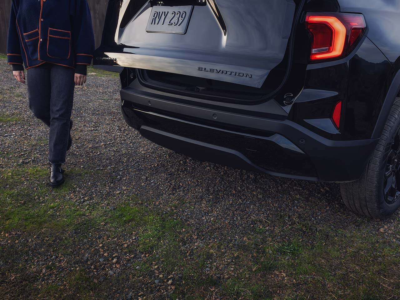 Vue arrière d’un SUV GMC noir 2027 à élévation terrain, avec le hayon ouvert à l’approche d’une personne.