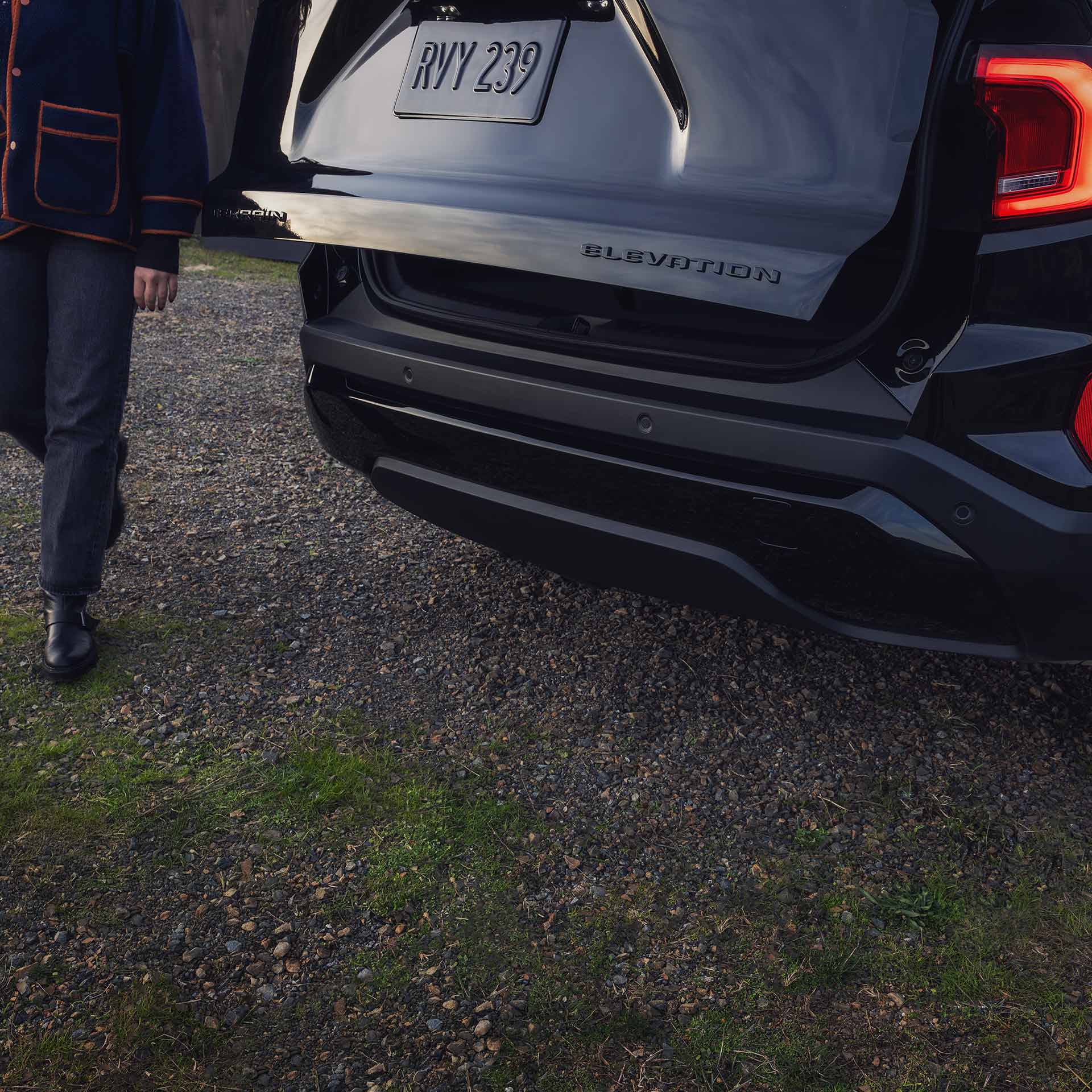 A Rear View of a Black 2027 GMC Terrain Elevation SUV with the Tailgate Open as a Person Approaches it.