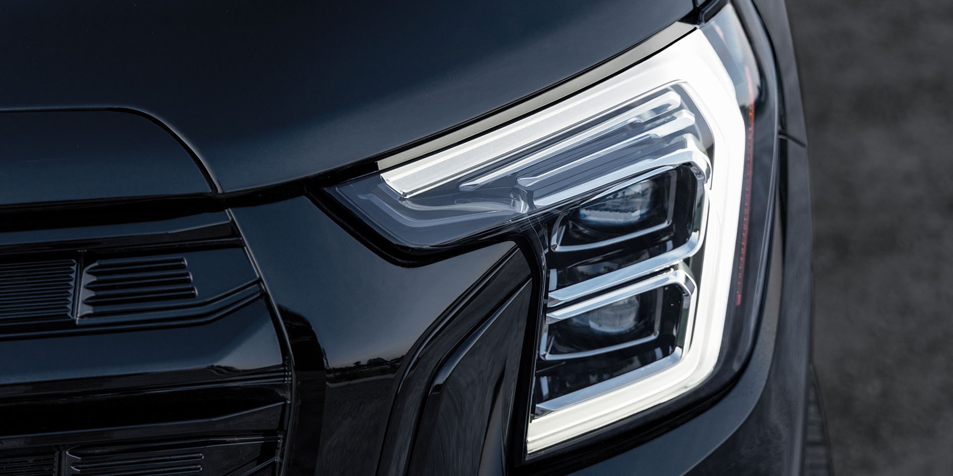 Un gros plan du phare LED moderne et de la calandre sombre d’un GMC Terrain noir 2027.