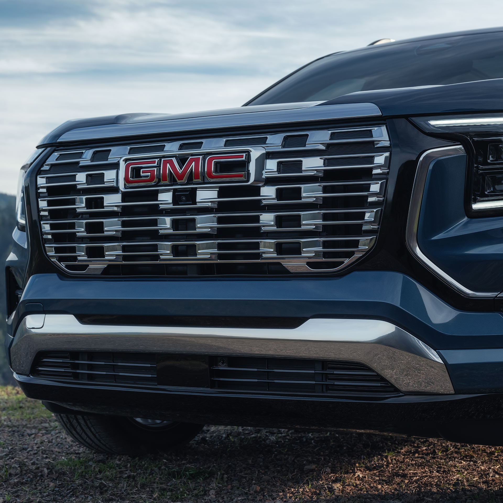 Un gros plan de la calandre chromée et du logo terrain rouge GMC 2027 sur l’avant d’un SUV bleu GMC Terrain 2027.