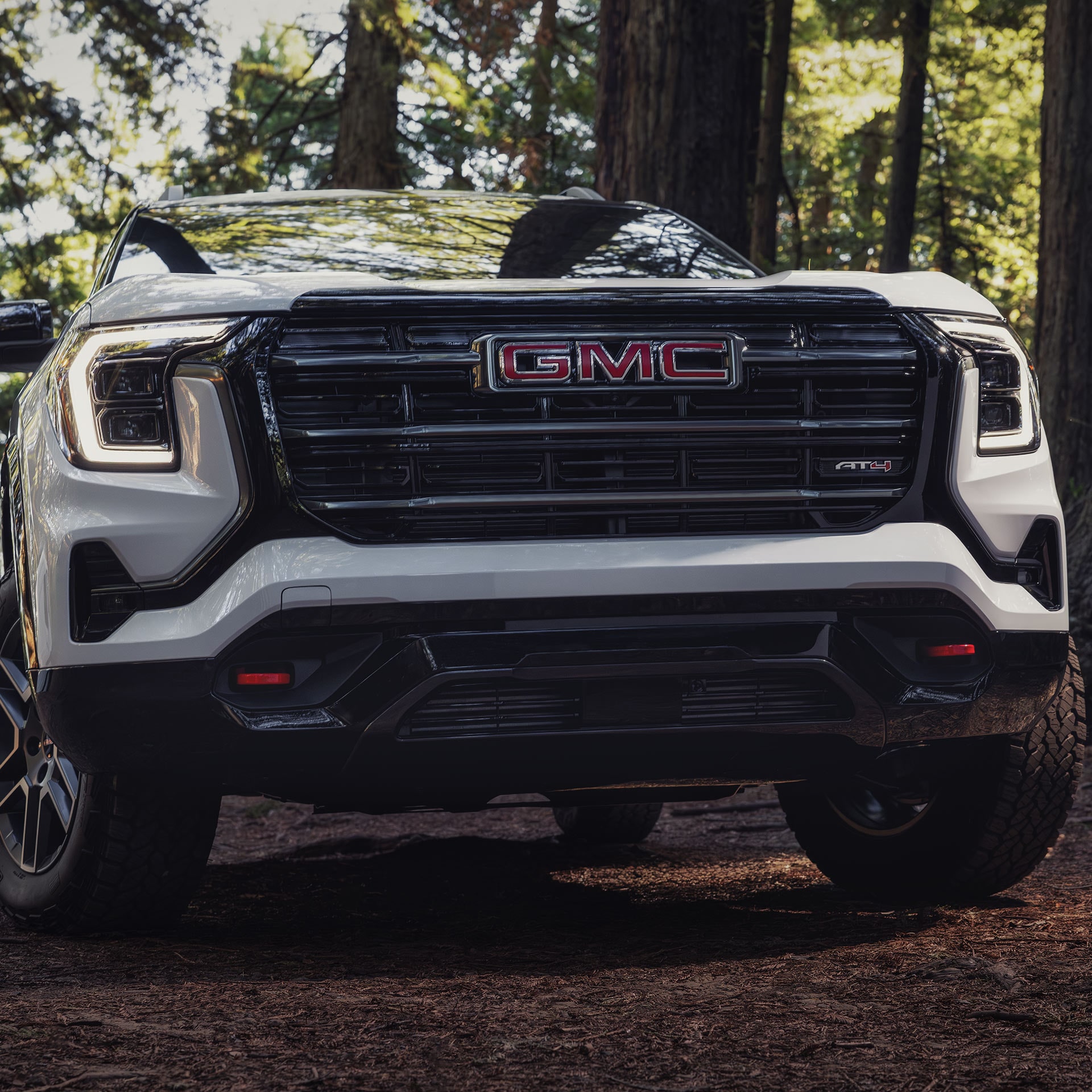Vue de face d’un SUV AT4 GMC Terrain blanc 2027 avec une calandre distinctive et des phares lumineux, garé sur un sentier forestier.