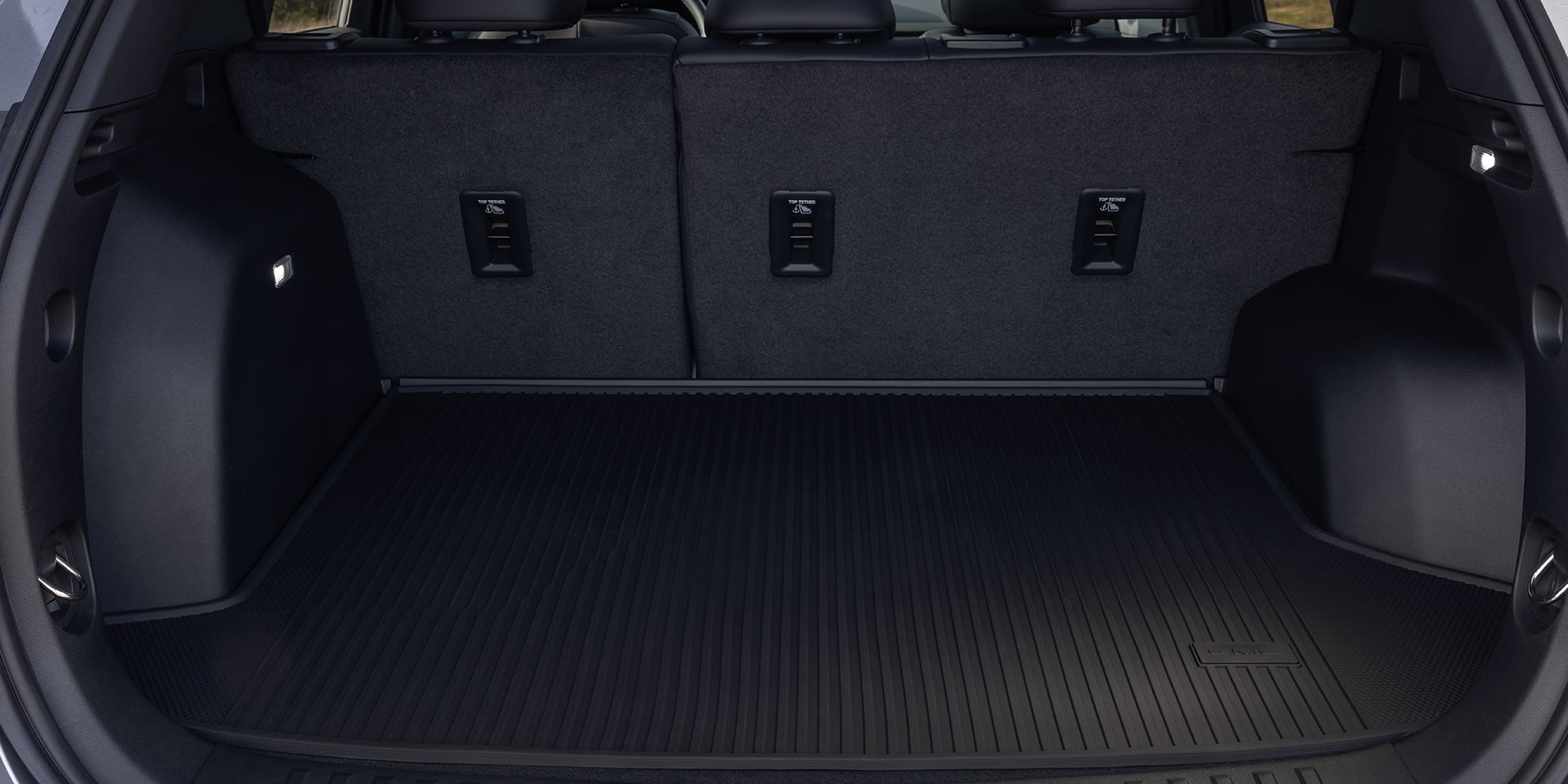 L’espace de chargement vide d’un SUV terrain GMC 2027 avec les sièges arrière relevés et un tapis en caoutchouc protecteur.