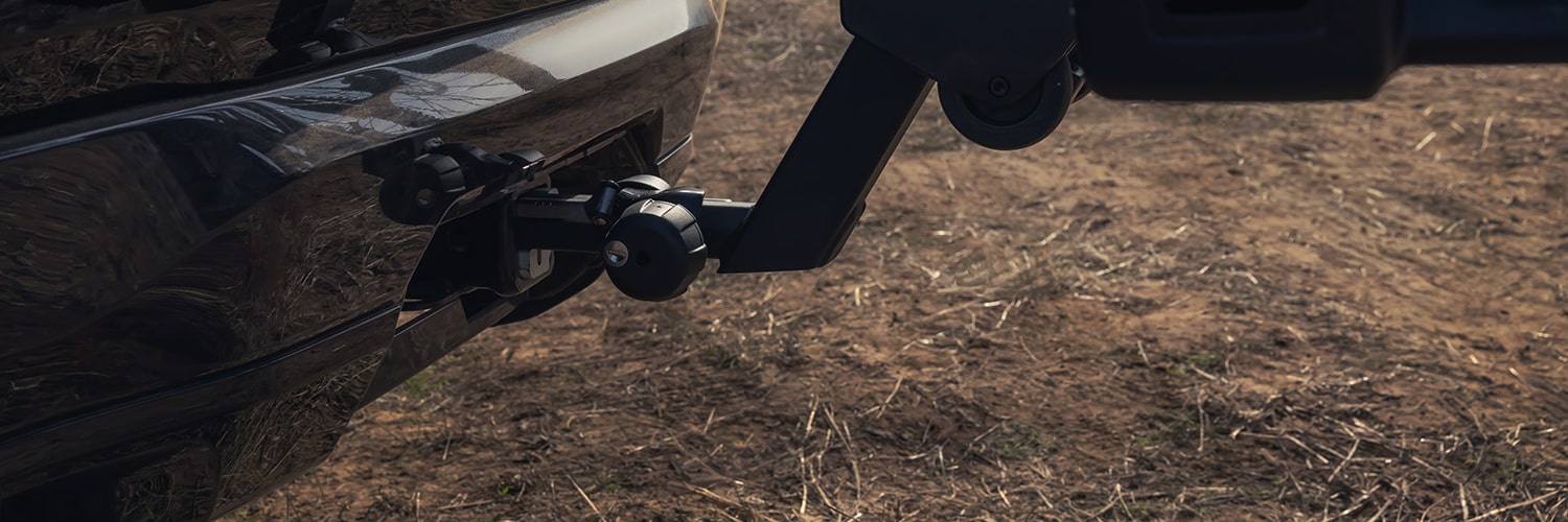 Vue rapprochée du pare-chocs arrière d’un SUV terrain GMC blanc 2027 avec un porte-vélos tenant une roue de vélo.