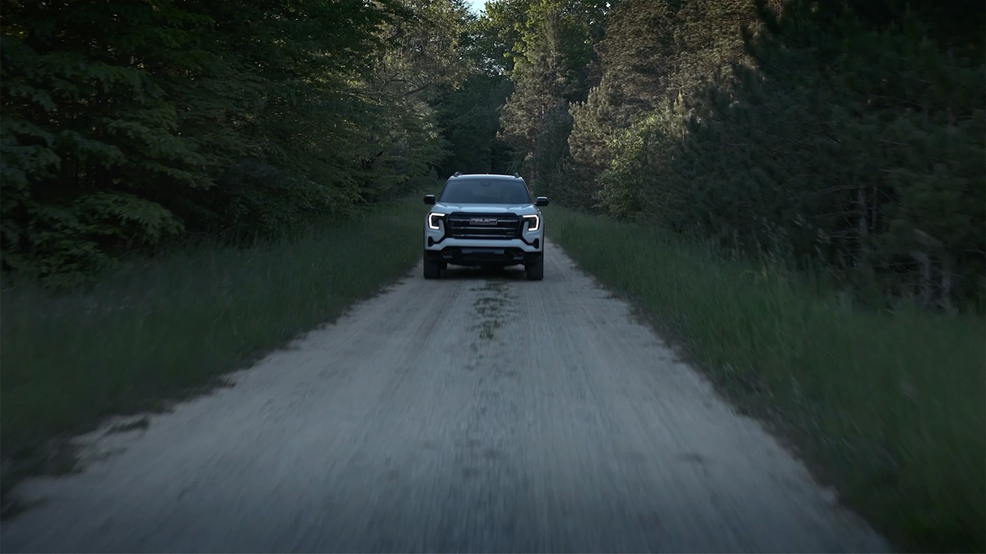 Un SUV terrain GMC blanc 2027 roulant de plein fouet sur une route de terre à travers une forêt dense.