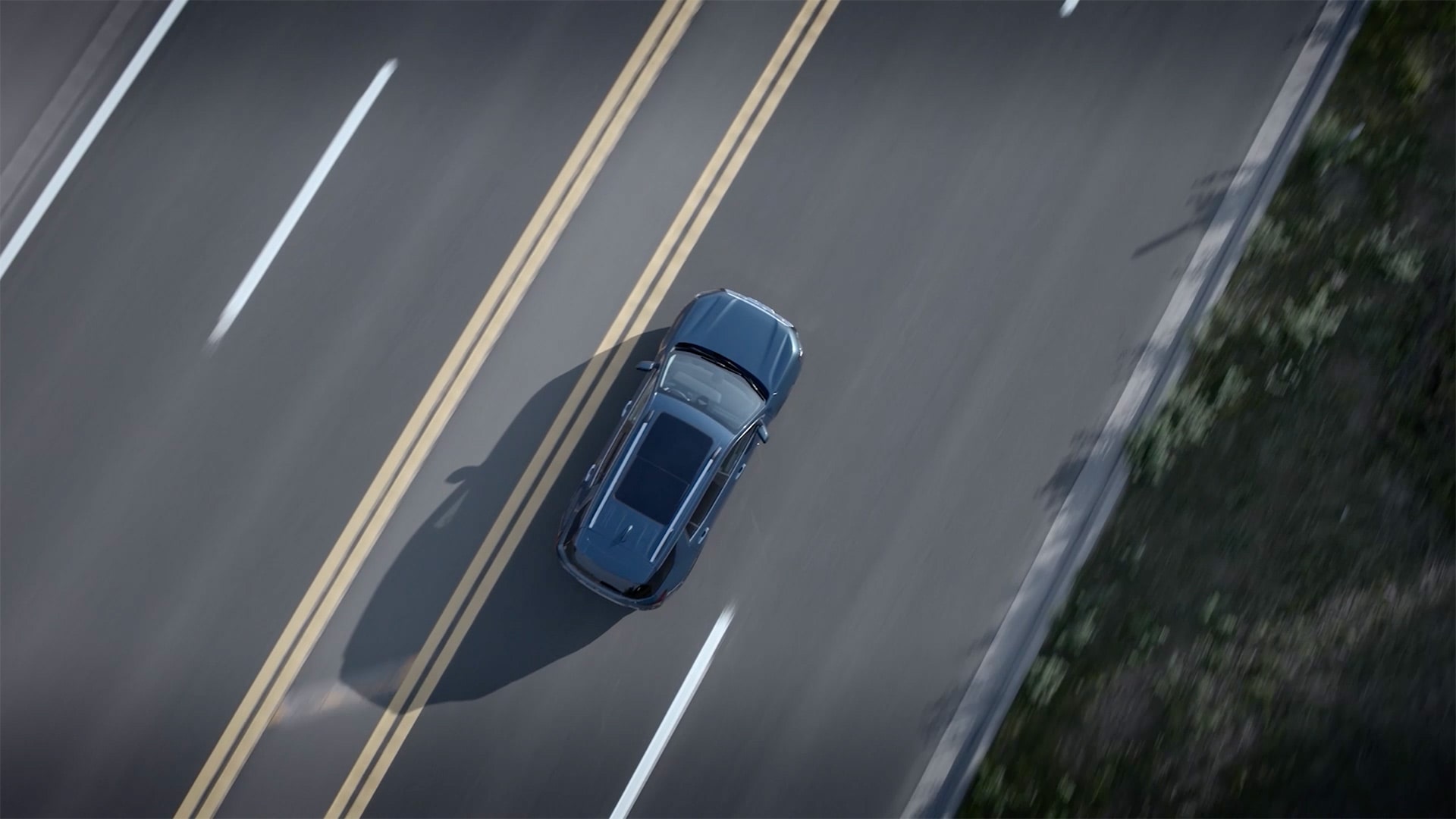 Vue aérienne d’un SUV GMC Terrain 2027 gris foncé roulant sur une route à plusieurs voies avec des marquages jaunes et blancs.