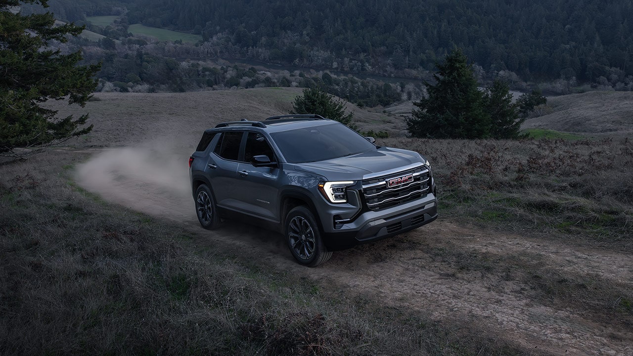 Un SUV GMC Terrain Denali gris 2027 soulevant de la poussière alors qu’il roule sur un sentier de terre à travers une vallée.