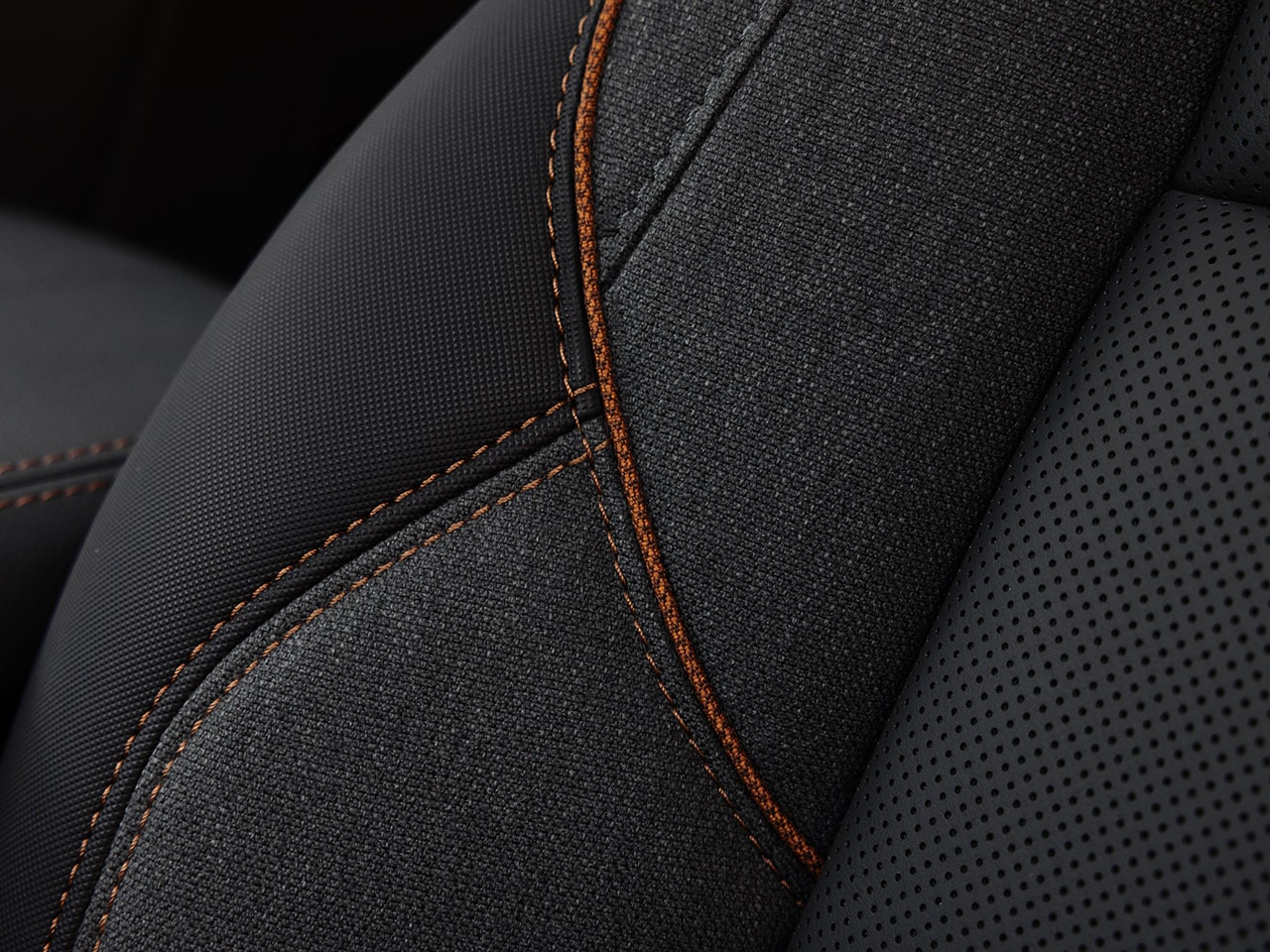 Gros plan d’un siège auto gris foncé avec tissu texturé, cuir perforé et coutures orange du GMC Terrain 2027.