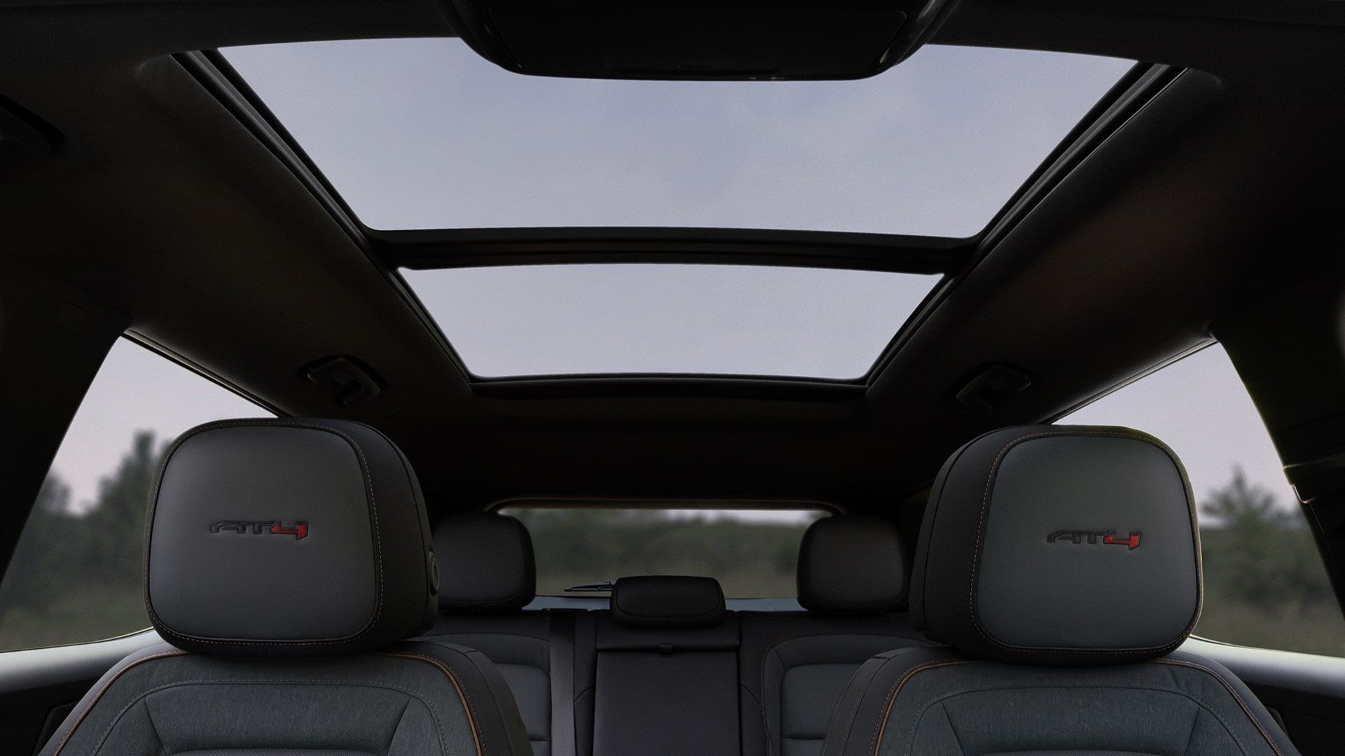 Vue intérieure d’un SUV terrain GMC 2027 avec des sièges AT4 gris foncé et un toit ouvrant panoramique.