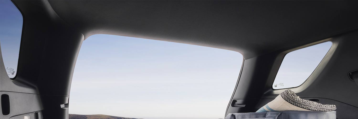 Équipement de camping incluant un matelas de couchage et un sac glacière dans le coffre d’un SUV GMC Terrain 2027 avec un paysage côtier au-delà.