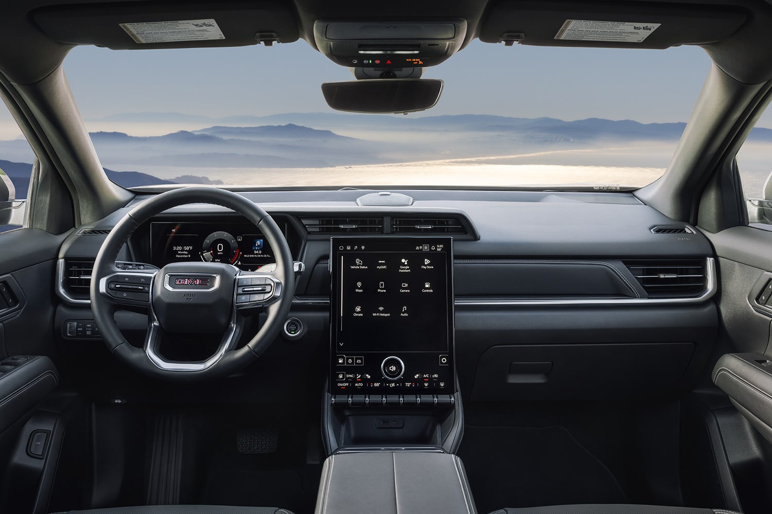 Vue intérieure d’un tableau de bord terrain GMC 2027 avec volant et écran d’infodivertissement surplombant les montagnes brumeuses.