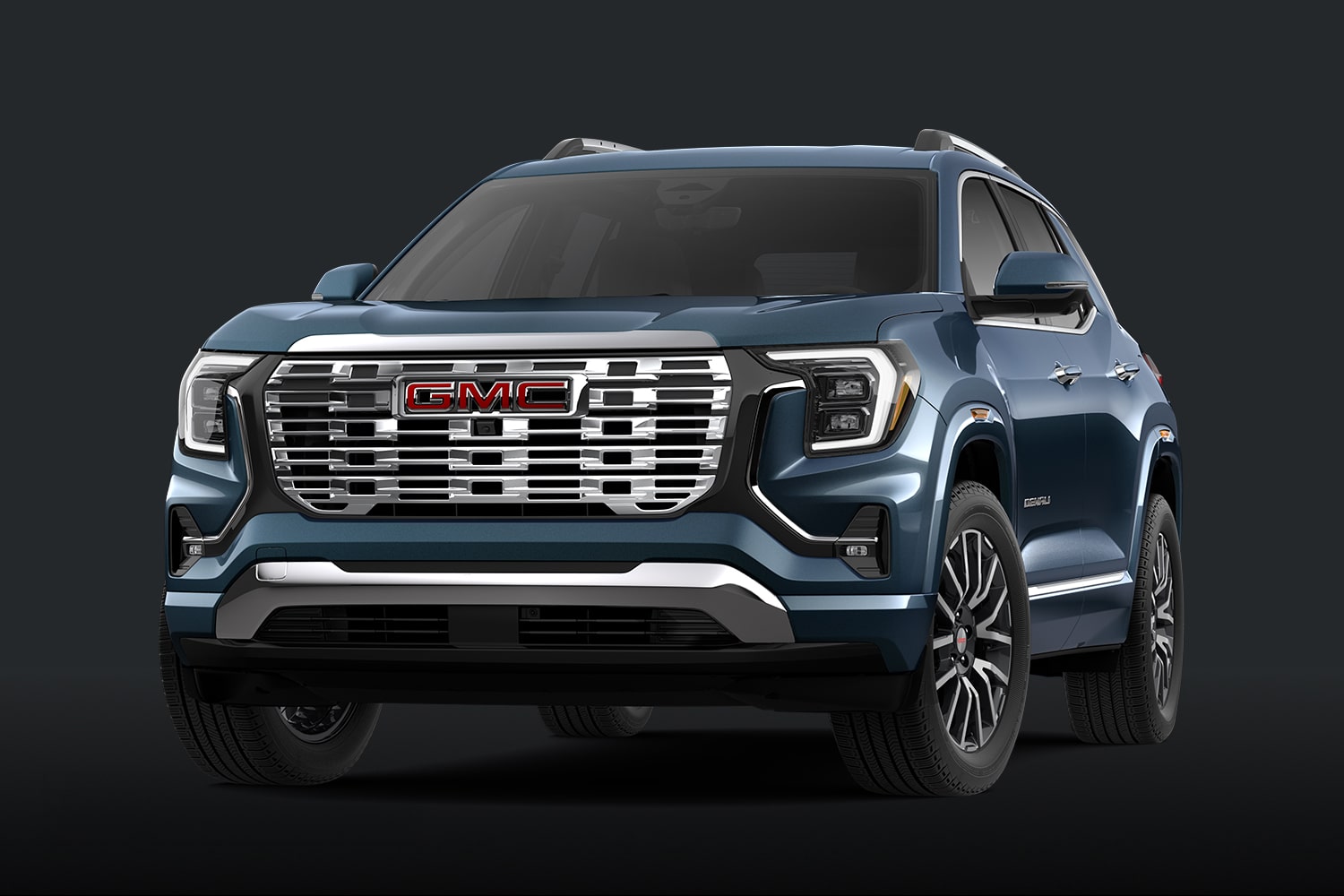 Un SUV GMC Terrain Denali bleu bleu bleu bleu avec une calandre chromée sur un fond sombre.