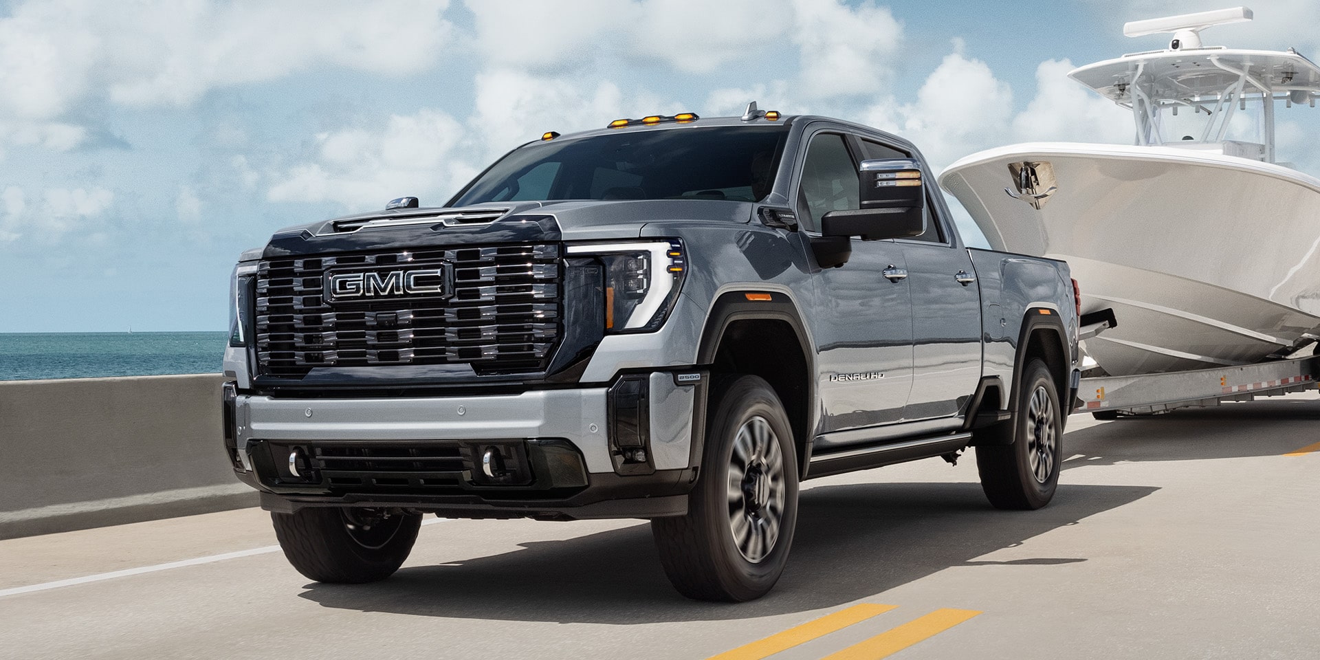 Vue latérale avant du GMC Sierra HD Denali Ultimate 2026 qui remorque un bateau sur la route.