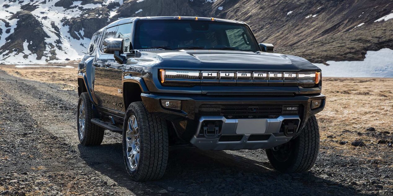Front-side view of the GMC HUMMER EV Pickup Truck driving down a dirt road with mountains in the background.