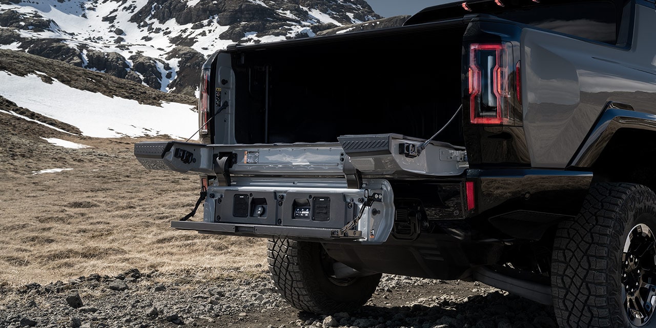 Close-up of the 2026 GMC Hummer EV Pickup Truck's Multipro Tailgate Open While Parked near a Snowy Mountain.