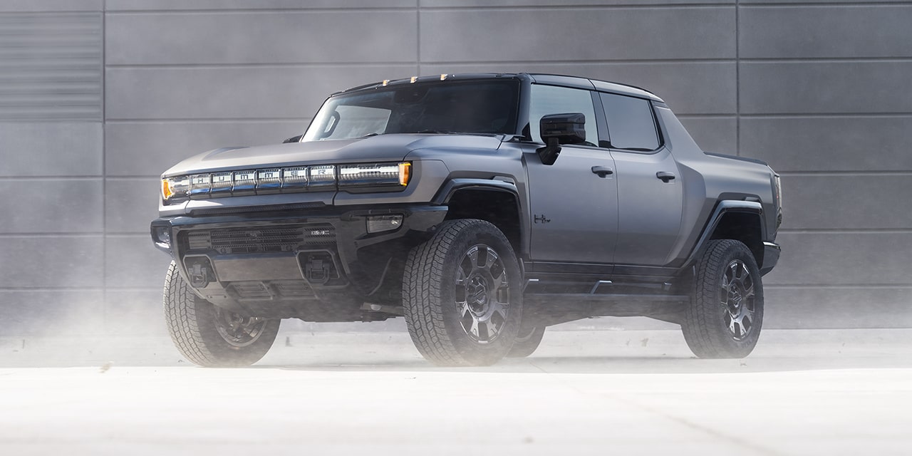 Front-Side View of a 2026 GMC Hummer EV Pickup Truck Parked by a Concrete Wall.