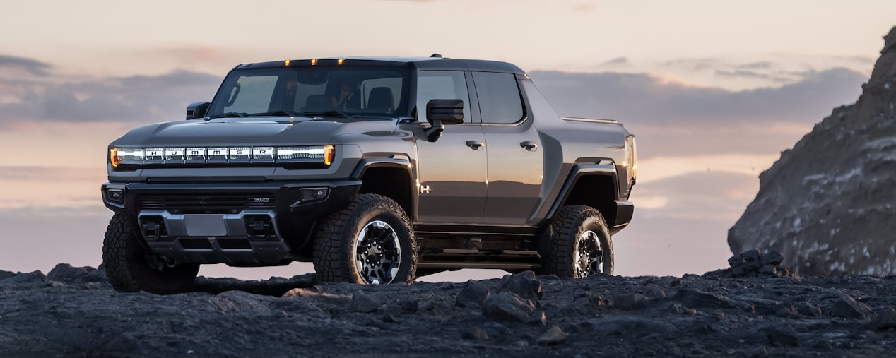 Front-Side View of the 2026 GMC Hummer EV Pickup Truck Parked on Top of a Rocky Mountain at Sunset.