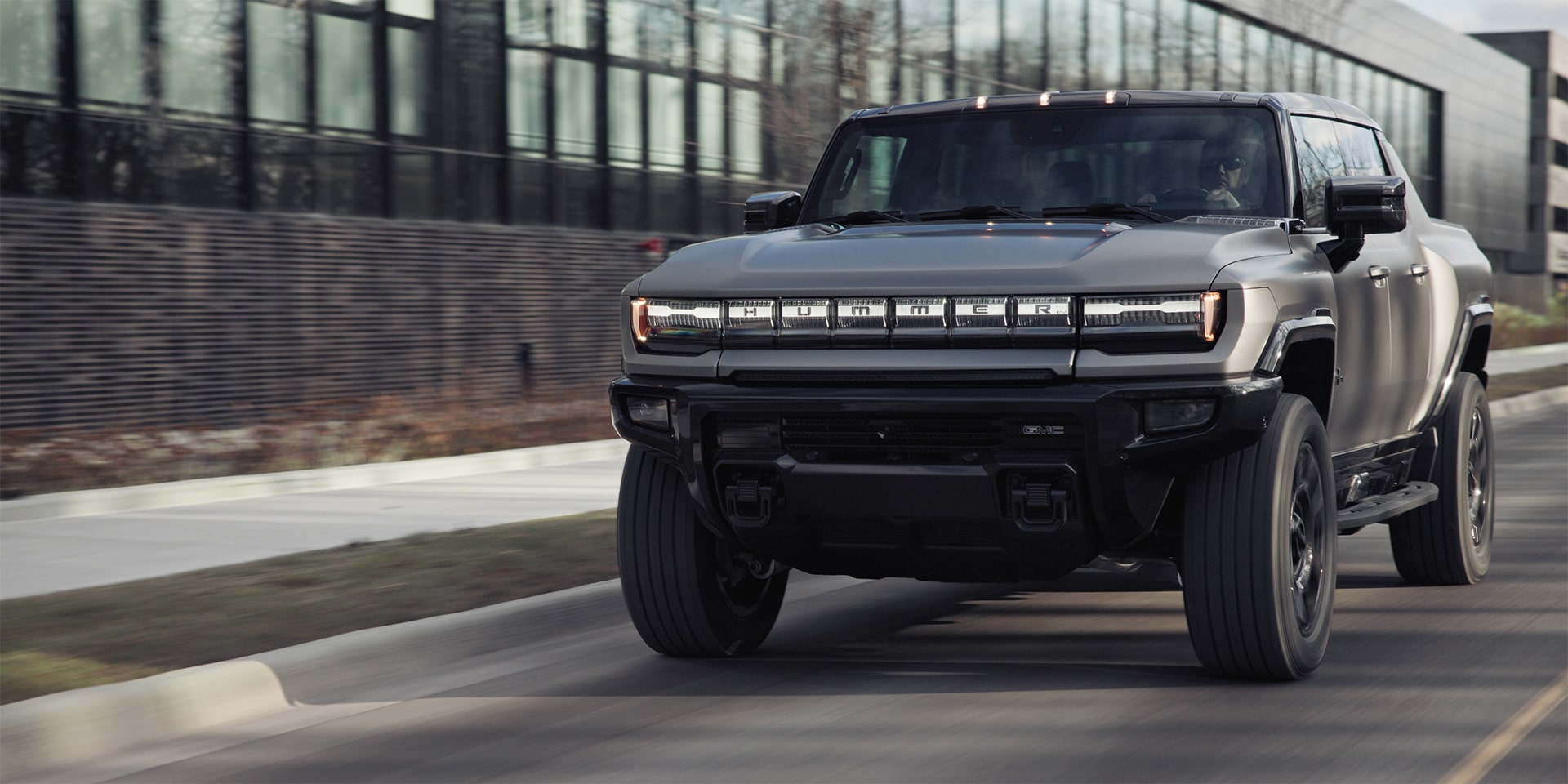The 2026 GMC Hummer EV Pickup Truck Driving Past a City Building.