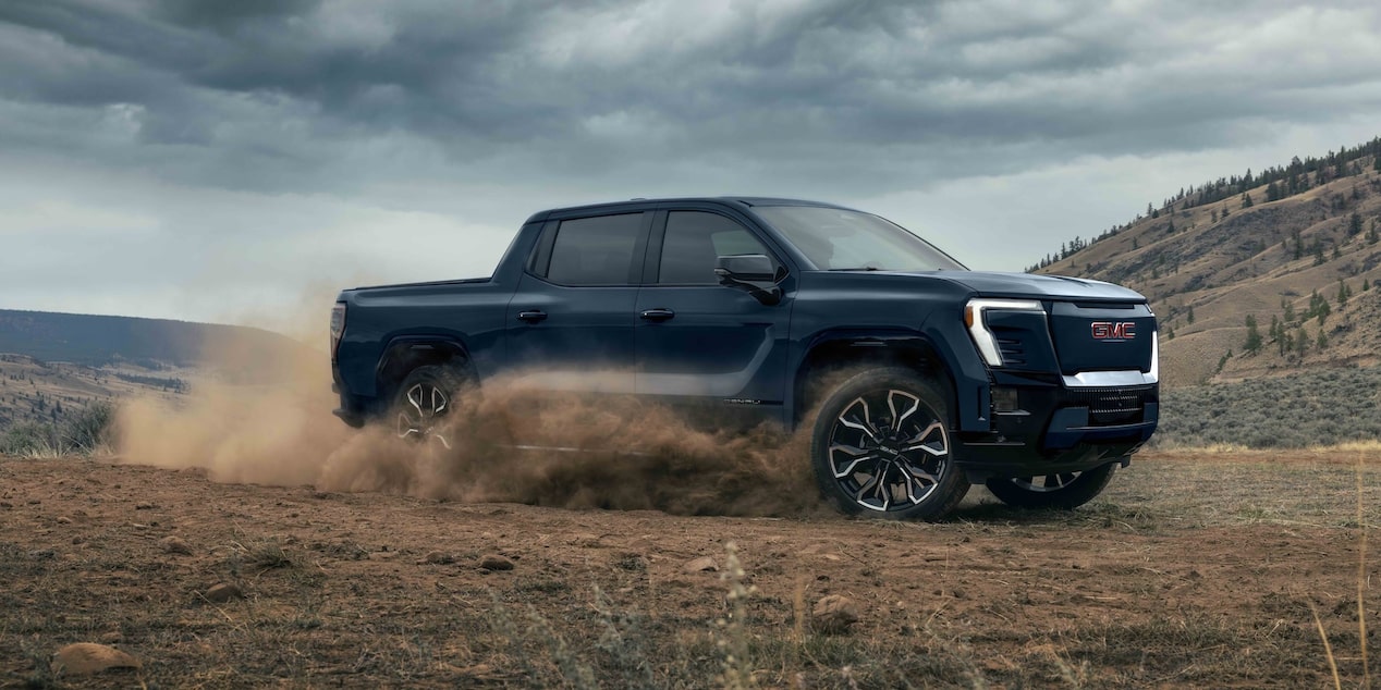 Vue latérale du GMC Sierra EV 2026 en conduite hors route dans les montagnes.