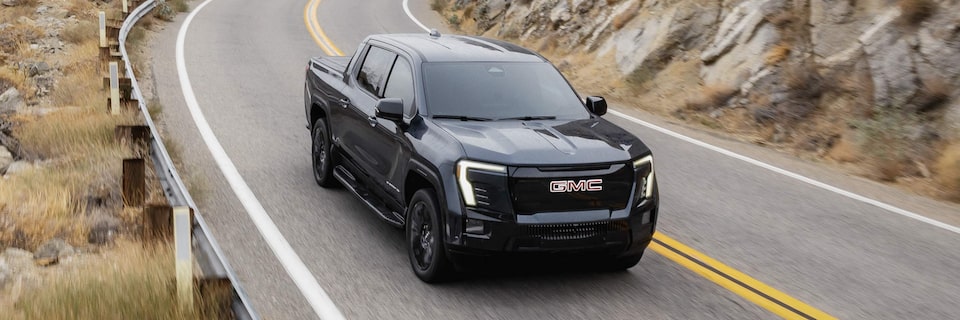 Vue latérale avant du GMC Sierra EV 2026 en mouvement sur une route de montagne.