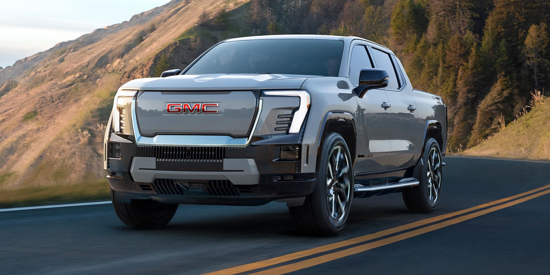 Le pick-up GMC Sierra EV 2026 en mouvement seul sur une route de montagne.