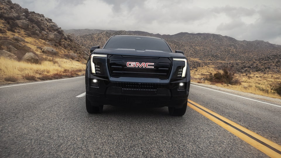 Vue avant du GMC Sierra EV 2026 en mouvement sur une route de montagne.