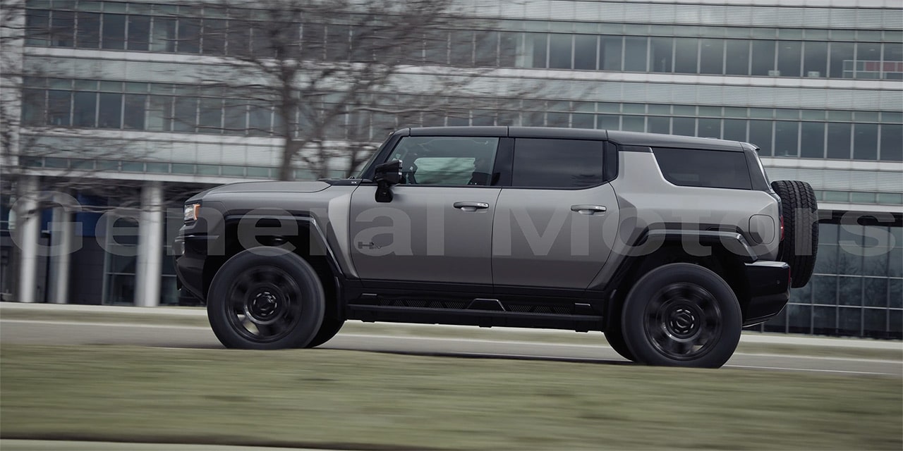 Side View of the 2026 GMC Hummer EV SUV Driving Past a Building.