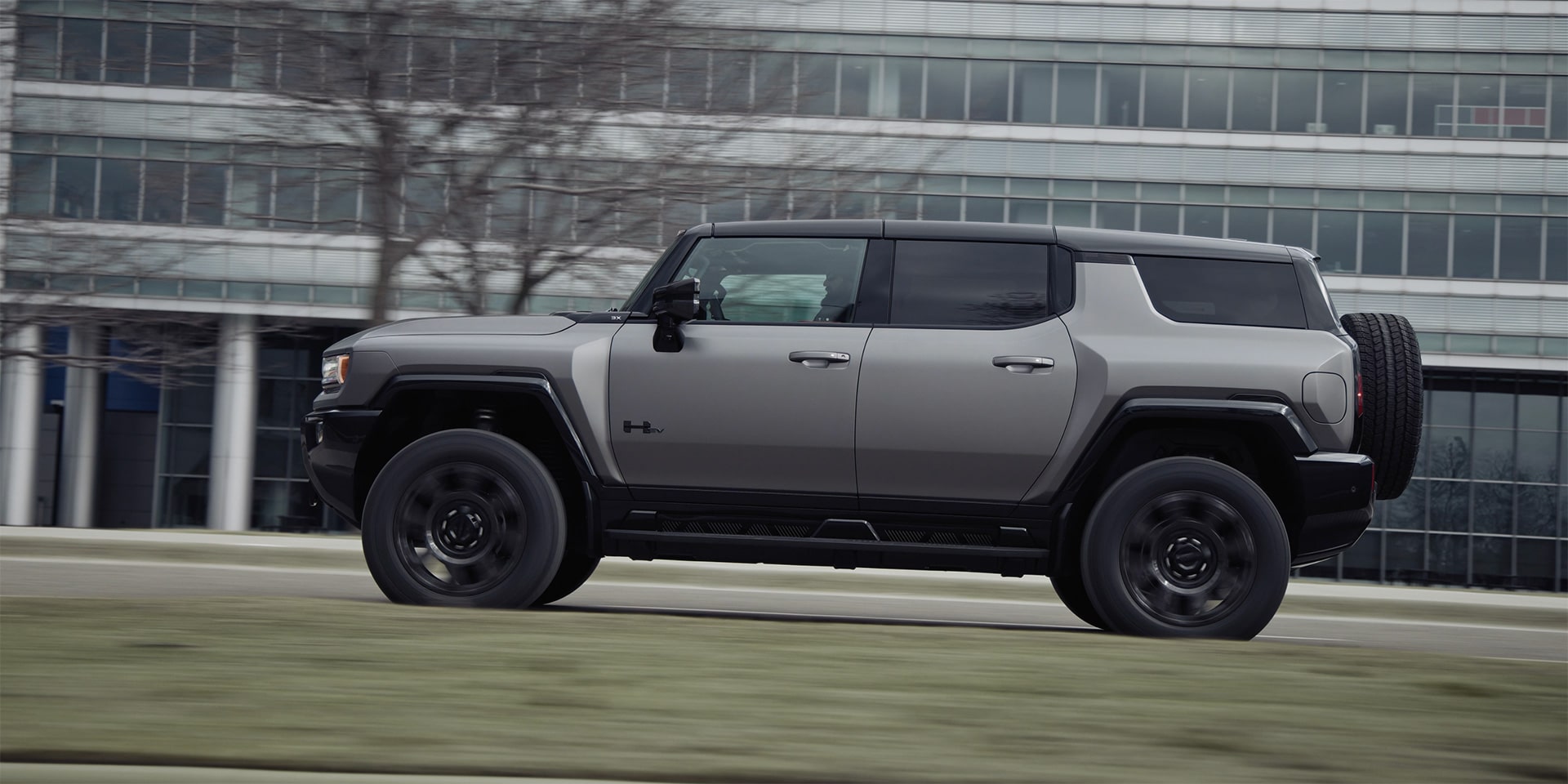 Vue latérale avant du VUS GMC Hummer EV 2026 en mouvement à côté d’un bâtiment.