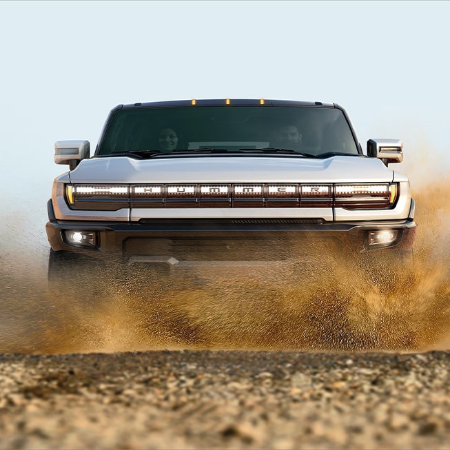 Front exterior view of the Hummer EV SUV driving through mud.