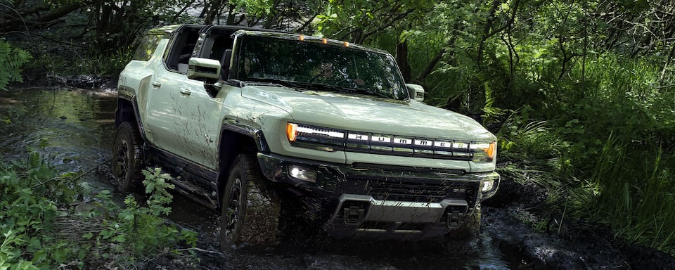 GMC Hummer EV SUV driving off road through a forest.