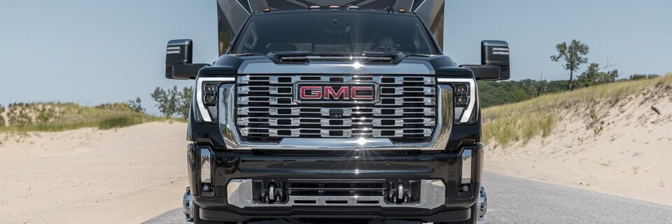 Front view of the 2024 GMC Sierra HD efficiently towing a trailer across a desert road.