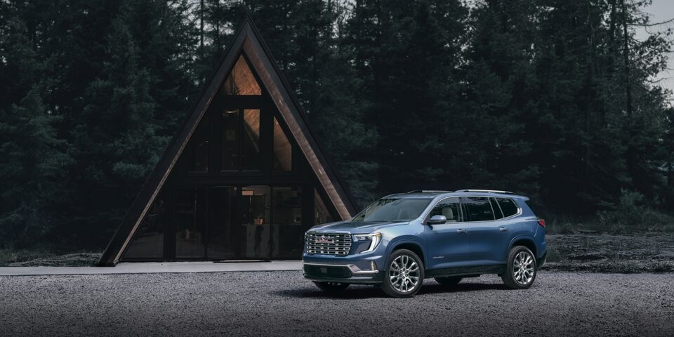 Vue latérale avant gauche du GMC Acadia stationné devant une maison moderne en bordure de la forêt.