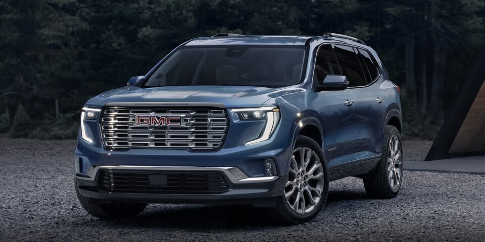 GMC Acadia Denali 2024 stationné sur du gravier devant des arbres.